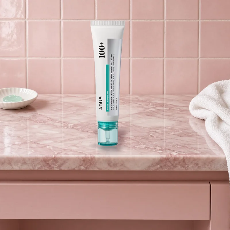 The ANUA PDRN Hyaluronic Acid 100 Moisturizing Cream tube on a pink marble vanity beside a dish of gel cream and a white towel