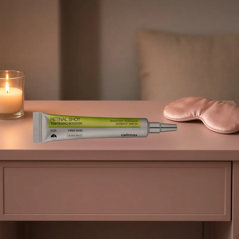 The celimax The Vita A Retinal Shot tube lying on a blush nightstand beside a lit candle and a silk sleep eye mask