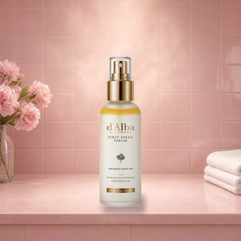 The d'Alba White Truffle First Spray Serum bottle on a blush vanity in a soft glowy mist beside pink flowers and towels