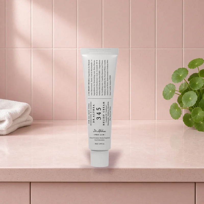 The Dr.Althea 345 Relief Cream tube standing on a blush tiled vanity beside fresh centella leaves and a white towel