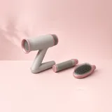 Illustration of a grey twist-style hair dryer with round brush and paddle brush attachments on blush