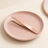 Illustration of rose gold slant tweezers on a pink dish